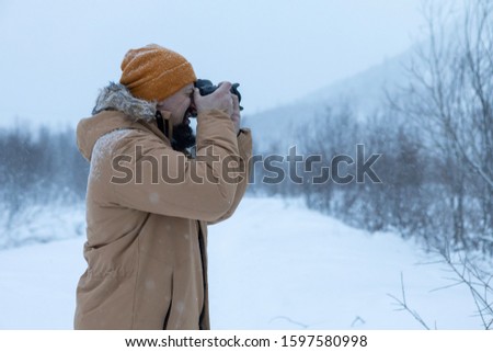 A man with a beard in the winter forest is making photographs. 