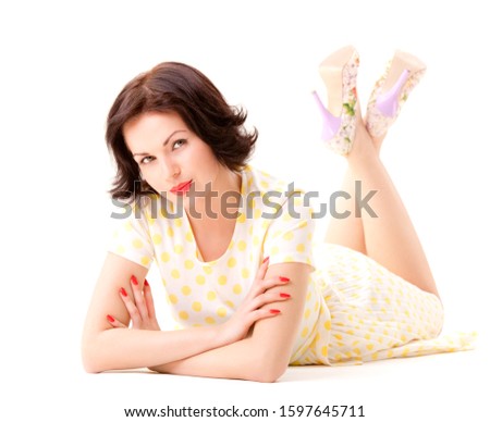 Young brunette woman in dotted dress and high heel shoes lying on floor over white background in photo studio. Fashion and beauty concept