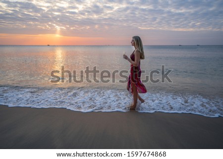 Beautiful blond girl walking on the beach in sunset with champagne glass in hand 