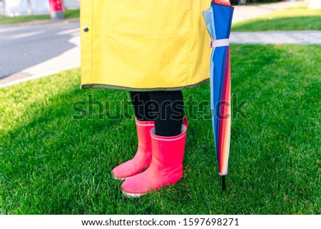 yellow raincoat. Rubber pink boots against. Conceptual image of legs in boots on green grass.