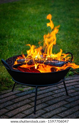 Making a fire in a fire bowl with burning wood, burning and orange colored flames makes is nice and warm outside Royalty-Free Stock Photo #1597706047