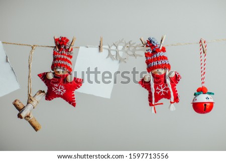 Red knitted christmas stars in funny hats. Christmas dolls and ornaments hanging on the rope with clothespin. White piece of paper for text.