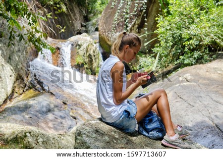 Young tourist woman with cellular phone checking geolocation and taking pictures. Rain forest in Thailand