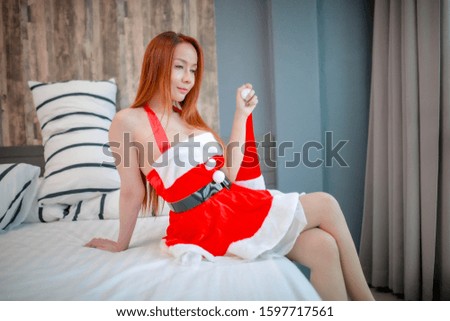  Merry Christmas and Happy New Year! Young woman in wear dress Santa Claus and in her bed.