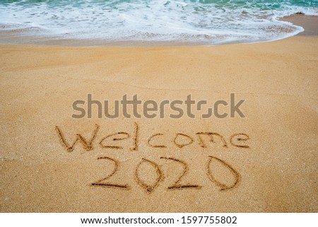 Welcome 2020 written in the sand with a wave erasing 2019- New Year’s concept
