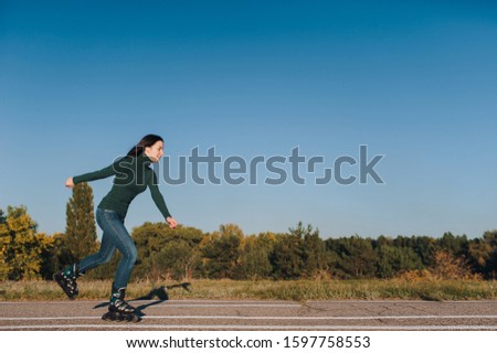 The girl rides on the rollers on the road in the park. Leisure and hobby of active people. Copy space.