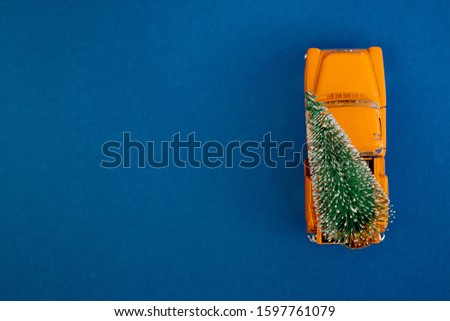 a miniature yellow car in the back carries a Christmas tree on a simple blue-aquamarine background, top view. Save the space. Concept, festive Christmas mood, gift delivery. The trend.