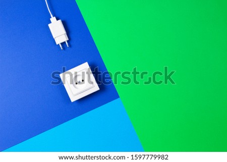 White electrical power socket and power plug on light blue, navy and green background. Top view, flat lay, copy space for text