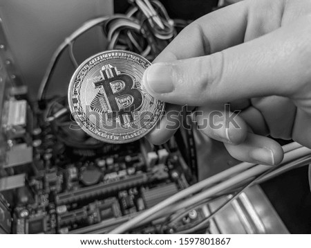 Holding a bitcoin in black and white among computer hardware, electronics and wires representing cryptocurrencies, mining and halving, and possibility of hacking