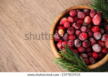 Cranberries in a wooden round Cup with fir branches on a wooden table to the right of the center with space for Your text or drawing