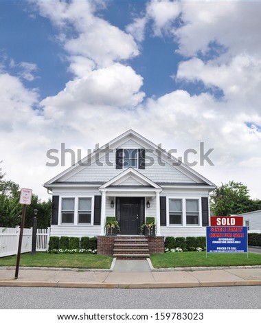 Sold Real Estate Sign on Front yard lawn of Suburban Bungalow Cottage Style Home Residential Neighborhood USA blue Sky Clouds