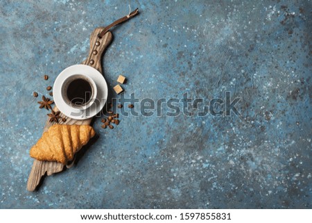 Top view of traditional french breakfast with croissant and coffee on wooden board and blue concrete background with copy space