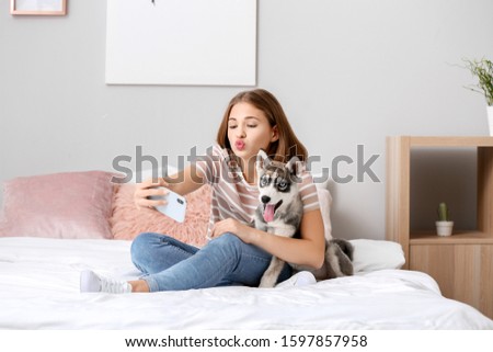 Cute teenage girl with funny husky puppy taking selfie on bed at home