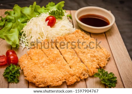 Japanese deep fried breaded pork cutlet served with shredded cabbage and tonkatsu sauce on wooden plate and black background. Stock photo