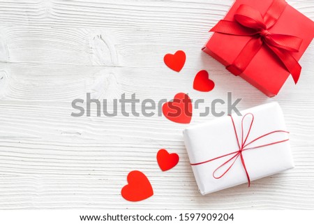 Present to a lover on Valentine's Day. Gift boxes near paper hearts on white wooden background top-down frame copy space