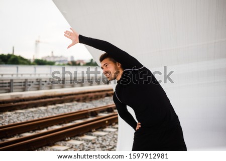 A handsome guy in a black T-shirt is training on the bridge