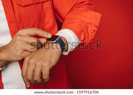Close up and cut view of man's hands. Hispanic or arabian guy point on black watches. Smart gadget and modern technologies. Point with finger. Isolated over red background