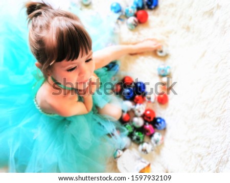 Little beautiful girl in a chic dress plays with Christmas toys and a garland in anticipation of the new year 2020. Little beautiful lady in a New Year's photo session.