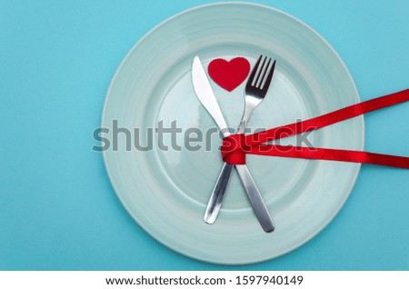 Concept layout for valentines day. Plate with cutlery on a blue background. Red hearts