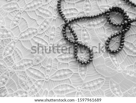 Black pearl beads on a delicate white lace background, flat lay, top view, romantic wedding still life