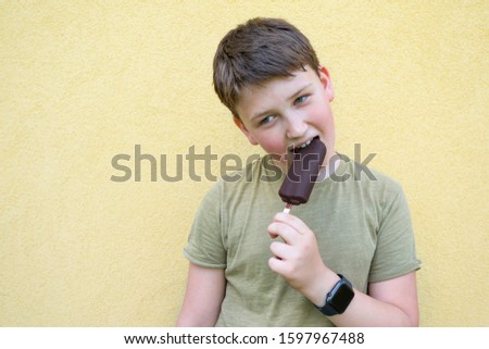 A teenager eats ice cream on a yellow wall background.