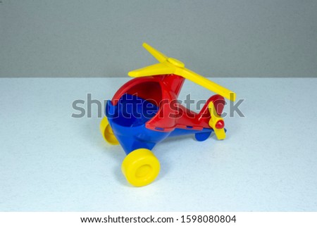 Children's toy, plastic red-blue helicopter with a yellow propeller and wheels on a gray fleecy background

