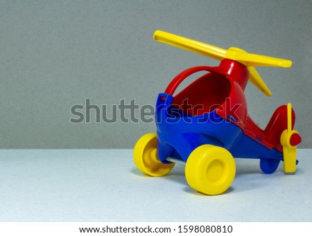 Children's toy, plastic red-blue helicopter with a yellow propeller and wheels on a gray fleecy background

