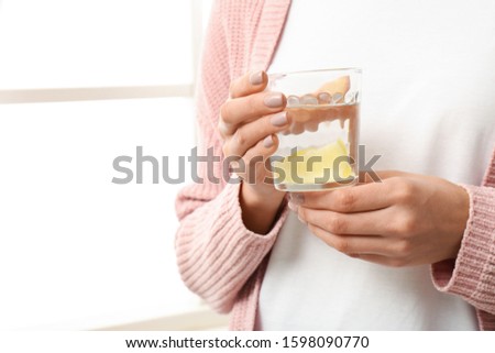 Woman with tasty lemon water near window, closeup