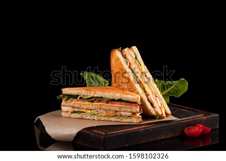 Two halves of a club sandwich on kraft paper. The filling of the sandwich consists of ham, cheese, tomato, chicken breast, sauce and fresh green salad. Royalty-Free Stock Photo #1598102326