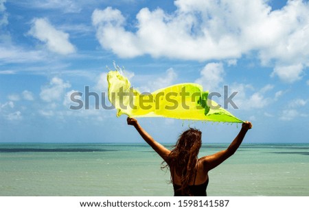Woman with red hair and curls holding a green scarf at the edge of the sea. Concept of loneliness, happiness, liberation and self-sufficiency. Photography with sunlight.
