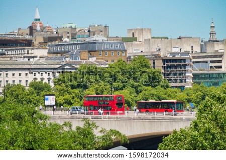 Two red buses crossing London Bridge on a beautiful summer day with city skyline on background.