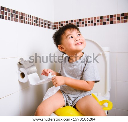 Asian little  kid 2-3 years old sitting on a kid bathroom accessory toilet and he play papers toilets