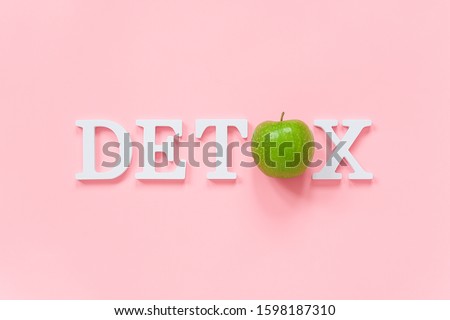Body detoxification and healthy diet concept. Green natural fresh apple in word DETOX from white letters on pink background. Creative flat lay Top view Copy space.