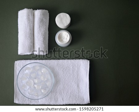 white cotton towels, face cream, cotton pads, ice cubes, spa on dark green background