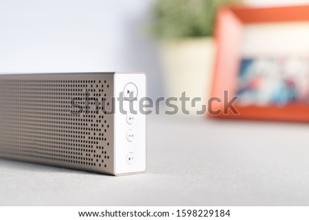 Closeup & Selective focus, modern and beautiful gold aluminium speaker on clean and tidy desk play calm, peaceful and relaxing music with red photo of couple and plant in background.