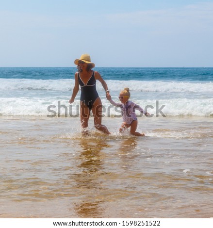 Happy mother girl go in water of ocean with big waves in the background