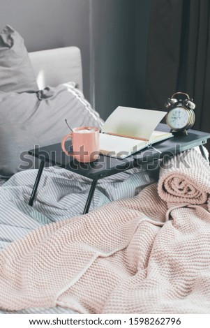 Coffee, daily, pencil on table on cosy grey bed and pink plaid for woman to plan day. Early morning. Remote work at home