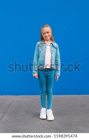 Little blond girl with blue eyes outdoors with blue background