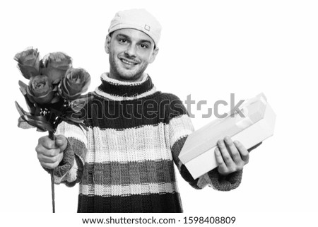 Studio shot of young happy man smiling while giving red roses and gift box