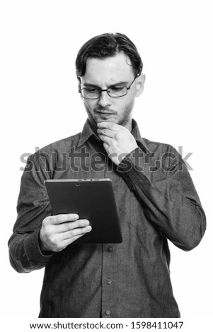 Studio shot of formal young man holding digital tablet while thinking