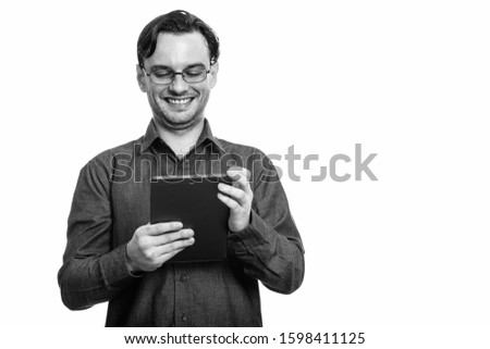 Studio shot of formal young happy man smiling while using digital tablet