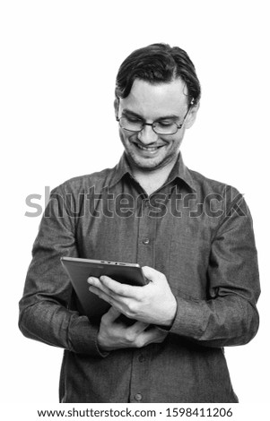 Studio shot of formal young happy man smiling while using digital tablet