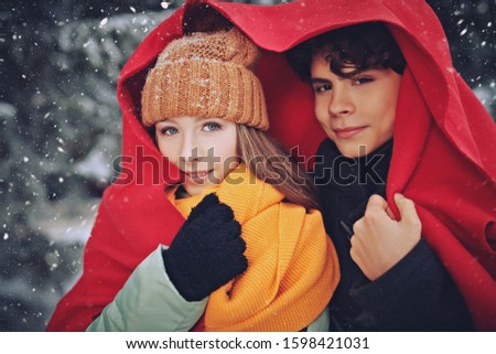 A young man and his girlfriend are standing, wrapped in a warm plaid, in a beautiful winter forest. Winter season, winter activities. First love.