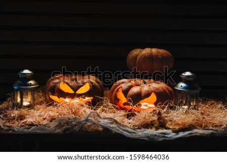 A smiling pumpkin lies on a straw, and lanterns stand and shine nearby