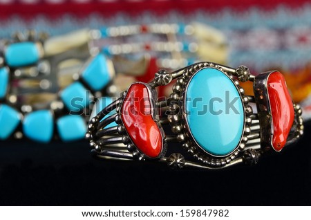 Selective focus on silver bracelet with turquoise and coral gemstones against background of several out of focus Indian artifacts.