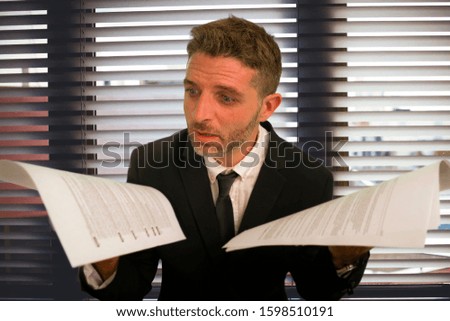 corporate office lifestyle portrait of stressed and frustrated business man holding paperwork reports overwhelmed and upset at modern office in work problems and stress concept