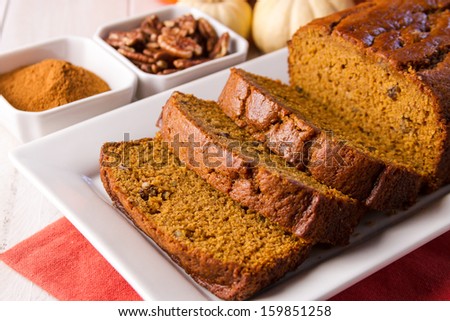 Sliced loaf of pecan cinnamon pumpkin bread sitting on white plate with orange napkin