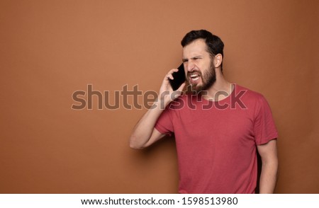Bearded man screaming in phone. Isolated brown background