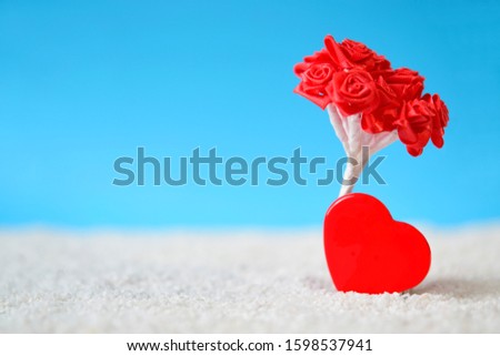 Beautiful red heart with bouquet of blurry red roses on white sand beach over blue clear sky background used for your design, for lover romantic symbol. Holiday, summer and valentine's day concept.