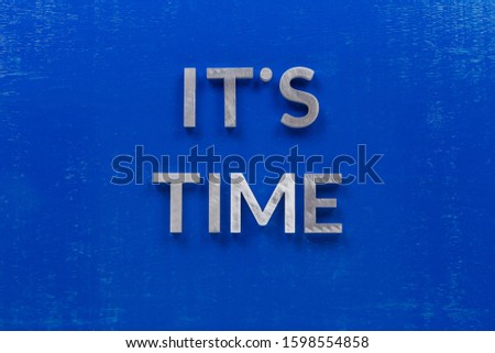 The phrase it's time laid on blue painted board with thick silver metal aphabet characters.